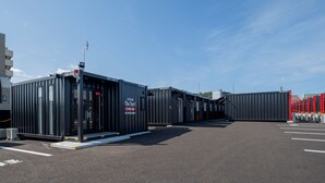 Un estacionamiento con varios contenedores de transporte, algunos con letreros que indican que se usan para almacenamiento u oficinas.