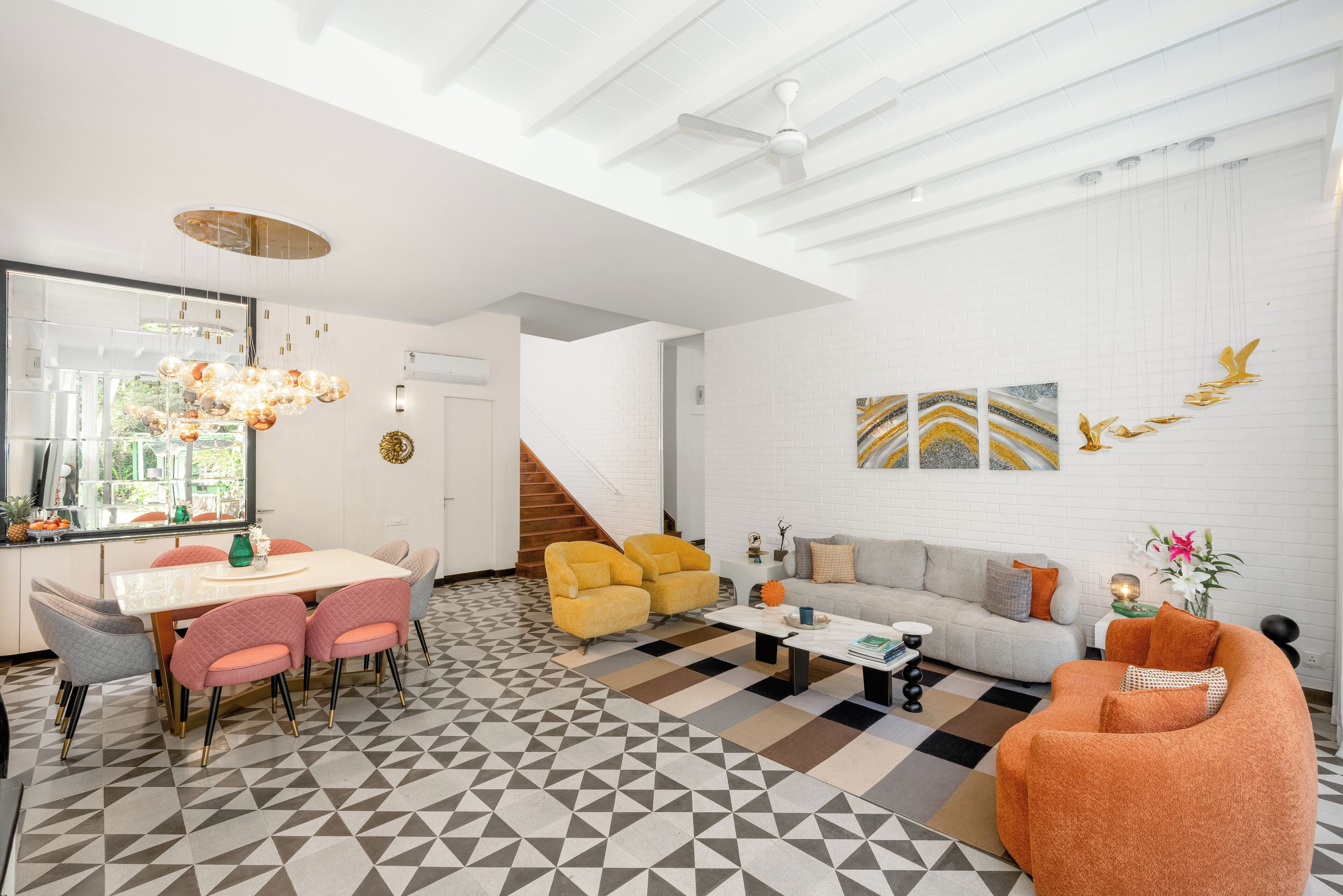 A modern living room with a sofa, coffee table, and chairs, a dining area with a table and chairs, and a staircase leading upstairs.
