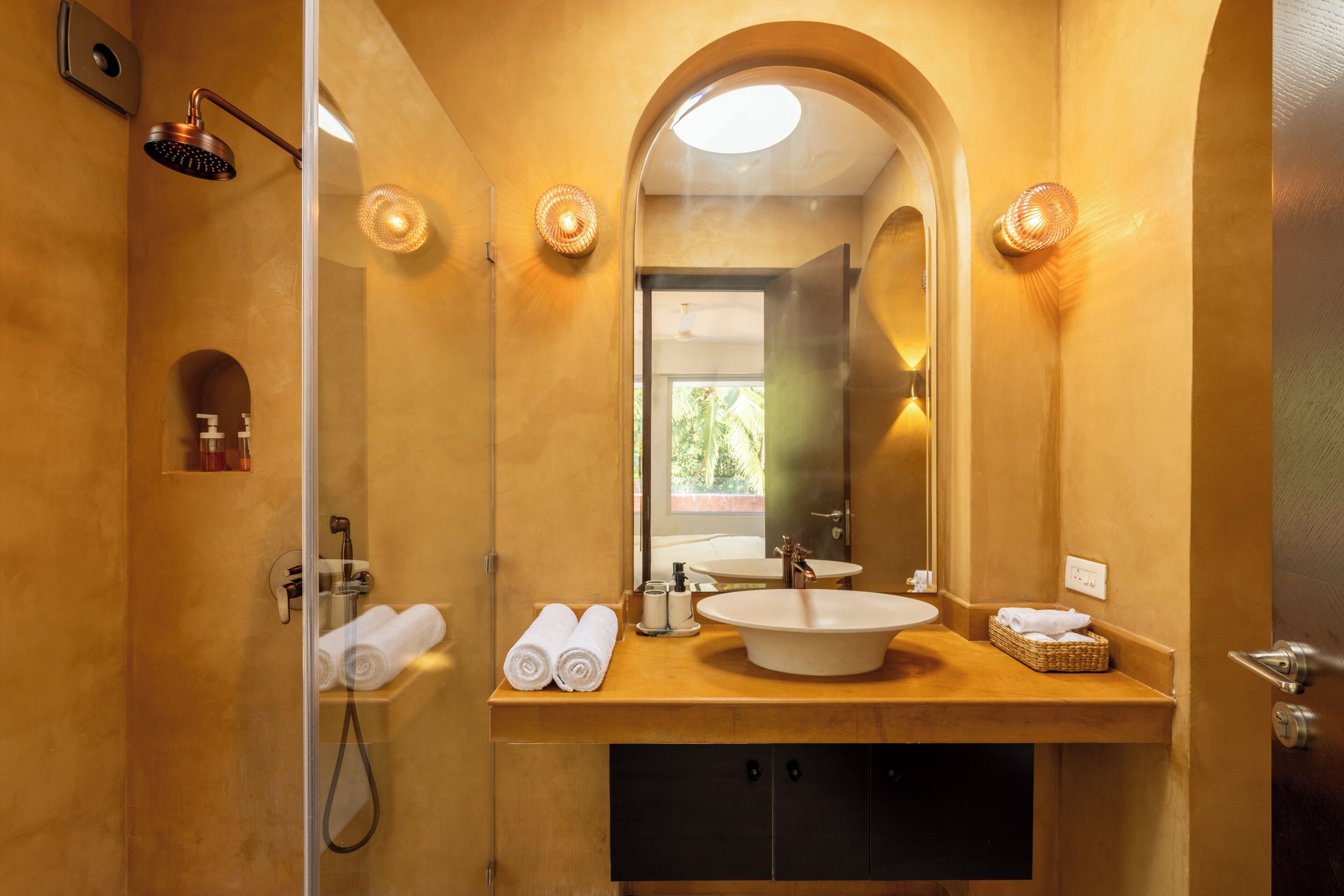 A bathroom with a large mirror, a sink, and a shower. There are towels and toiletries on the counter.