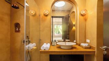 A bathroom with a large mirror, a sink, and a shower. There are towels and toiletries on the counter.