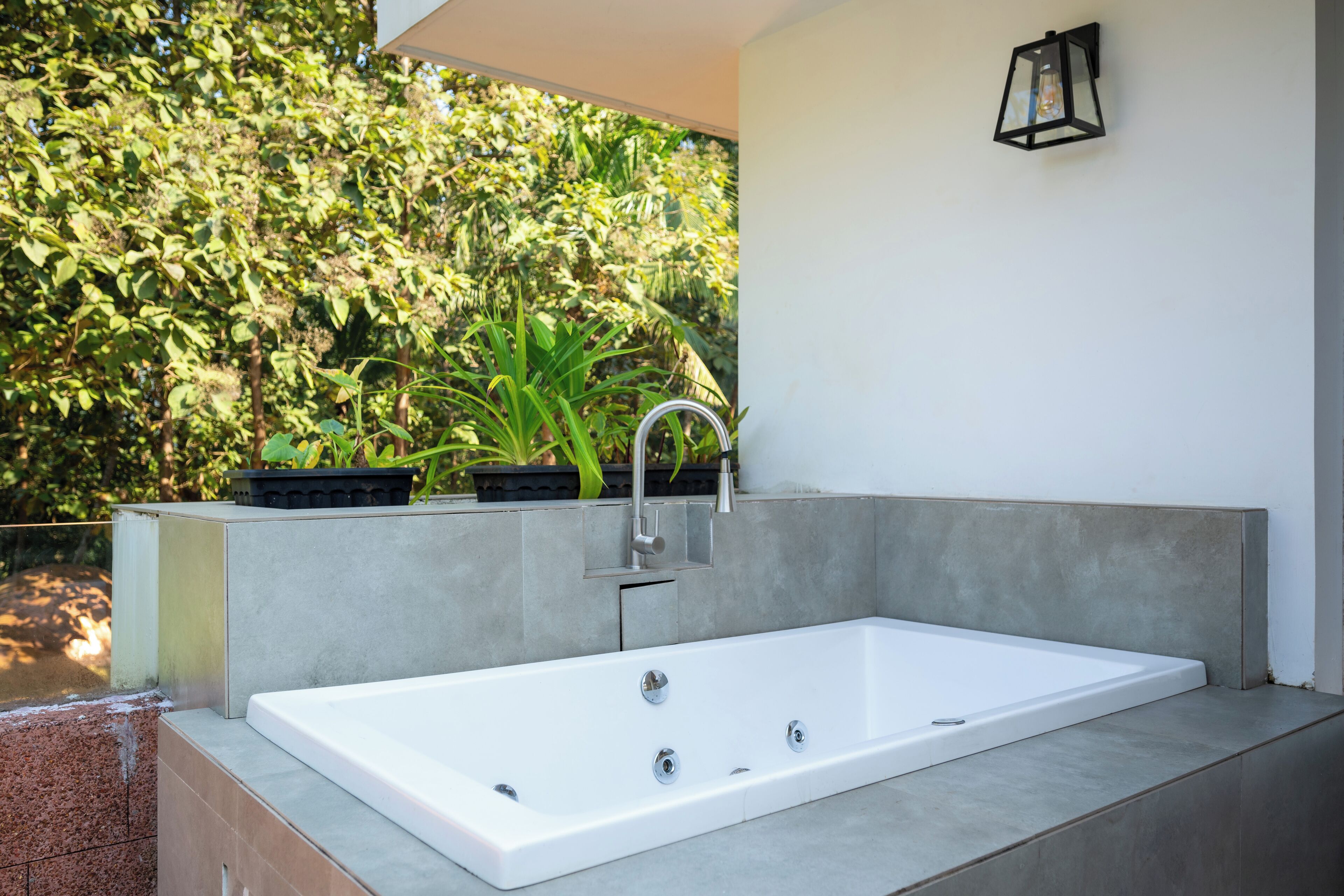 A modern outdoor bathtub with a faucet and a wall-mounted light fixture.