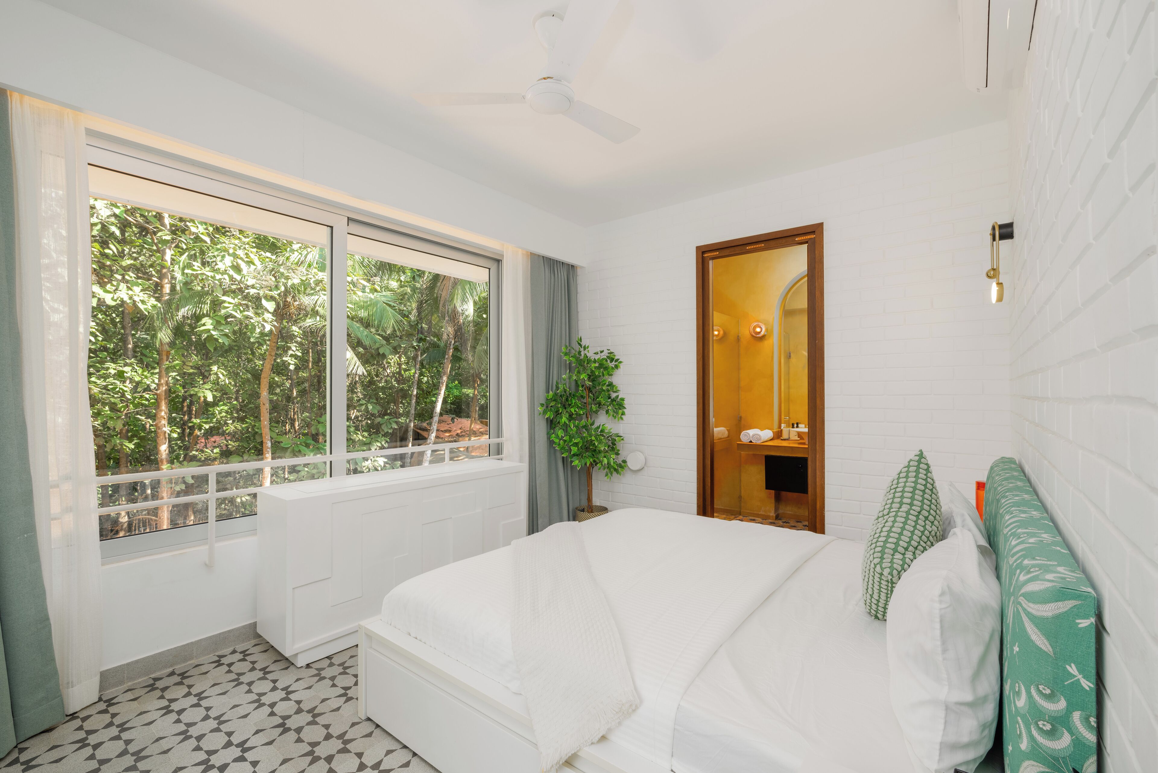 Un dormitorio con cama, ventana con vistas a árboles, ventilador de techo y mesita de noche.