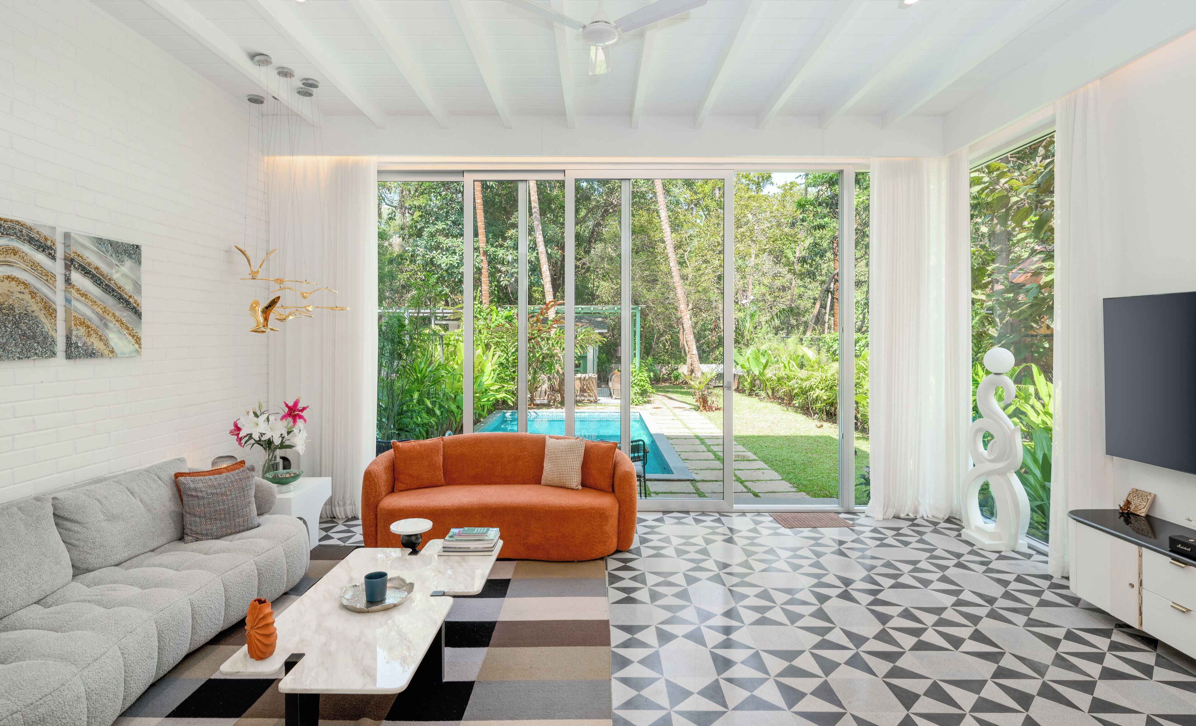 Ein modernes Wohnzimmer mit einem grauen Sofa, einem orangefarbenen Sessel, einem Couchtisch und einem Fernseher rechts.