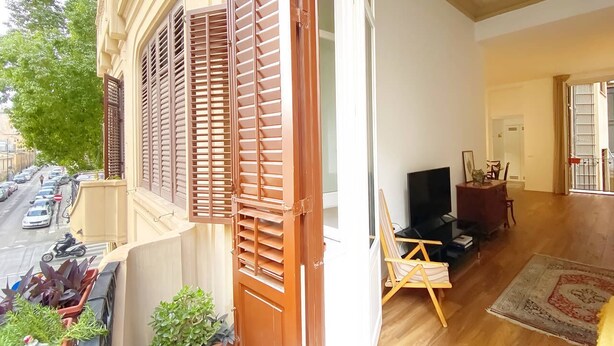 A balcony with wooden shutters, a TV, and a painting on easels, with a street view in the background. - Solemar Sicilia - Casa Castiglione (Palermo)