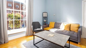 Un soggiorno con un divano e una poltrona grigi, un tavolino da caffè e una libreria alta di colore nero.