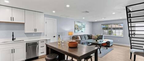 A modern kitchen with white cabinets, a dining area with stools, a sofa, and a coffee table.