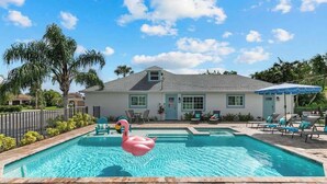 Une piscine avec un flotteur en forme de flamant rose, des chaises longues et une maison en arrière-plan.