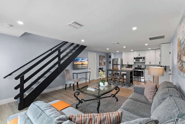 A modern living room with a staircase, a dining area, and a kitchen. - 541 SeaClusion Cottage| Pool&Spa | 5 Blox to Beach (Naples)