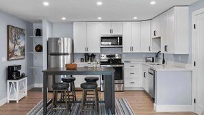 Une cuisine moderne avec des meubles blancs, des appareils en acier inoxydable, un îlot central doté de tabourets et un tapis à rayures.