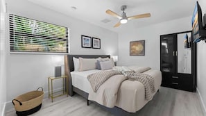 Un dormitorio moderno con cama, mesitas de noche, ventilador de techo, ventana con persianas y armario.