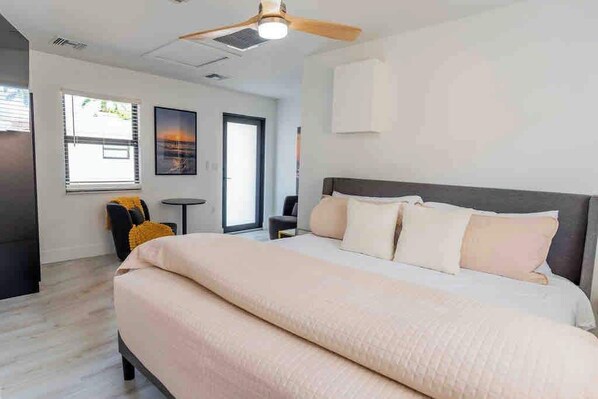 Een moderne slaapkamer met een groot bed, een plafondventilator, een kleine tafel en een raam met zonwering.