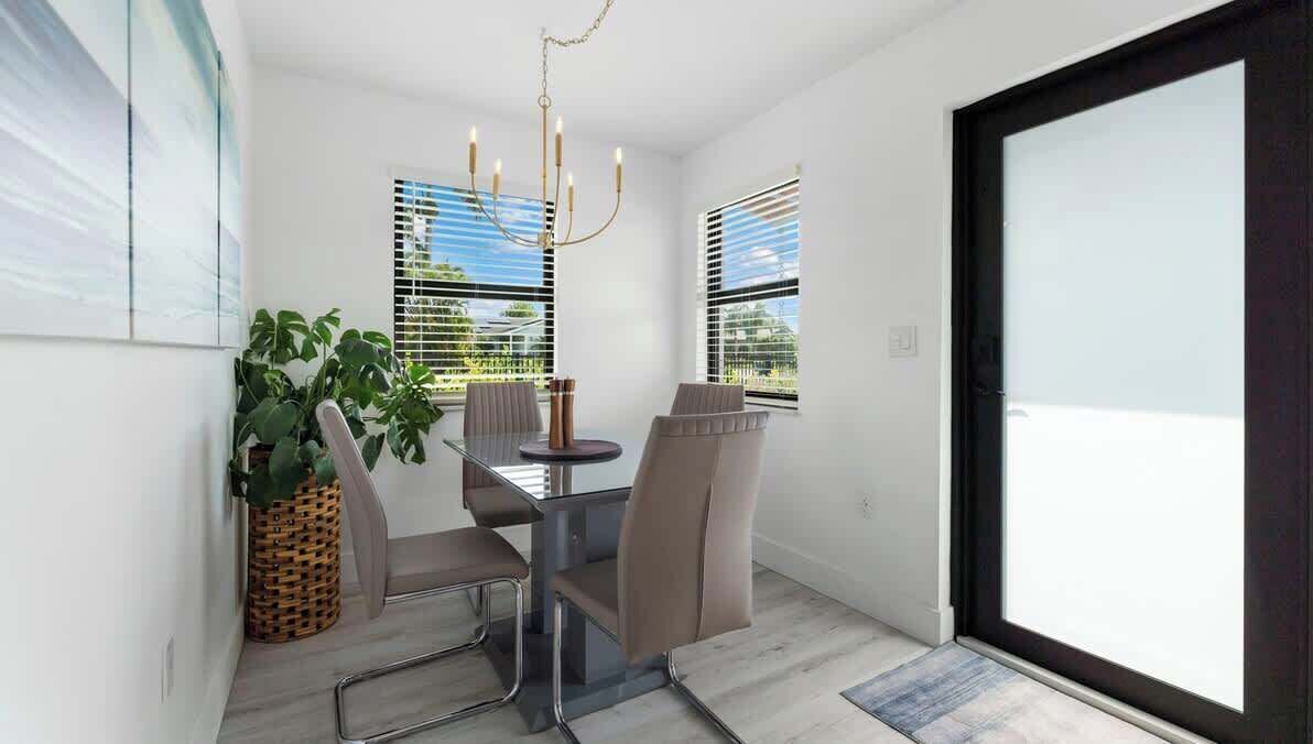 A dining area with a glass table, four chairs, a chandelier, and a potted plant.