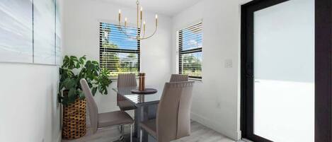 A dining area with a glass table, four chairs, a chandelier, and a potted plant.
