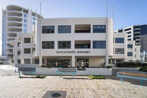 A modern building labeled "Oceanside Resort" with a wooden boardwalk in front, benches, and a clear sky.