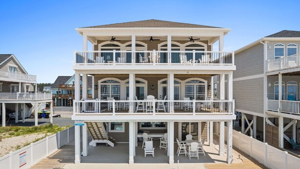A two-story beachfront house with a balcony, a pool, and outdoor seating.