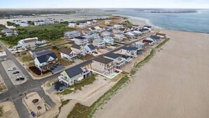 An aerial view of a coastal residential area with houses, a beach, and a road.
