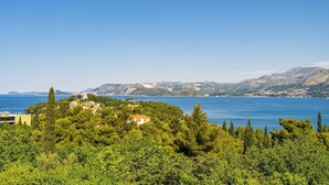 A coastal landscape with a view of the sea, a cluster of buildings, and a mountainous backdrop.