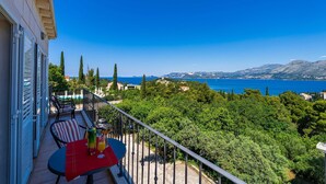 A balcony with a table and chairs, overlooking a mountainous landscape and a body of water.