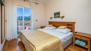 A bedroom with a bed, a nightstand, a bedside table, a window with curtains, and a view of a balcony.