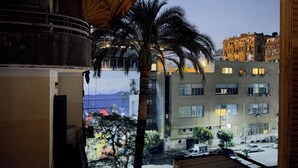 A view from a window overlooking a street with buildings, a palm tree, and parked cars. - One Season Hostel (Cairo)