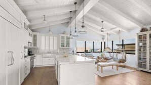 Una cocina amplia con armarios blancos, una isla grande y lámparas colgantes.