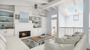 Un salón amplio con chimenea, muebles blancos y un balcón con barandilla.