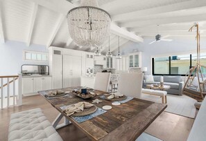 A spacious kitchen with white cabinetry, a wooden dining table set with plates and a tray of food, and a large chandelier. - Oceanview 2,200 SF Home | Steps to Beach | Gym (Manhattan Beach)