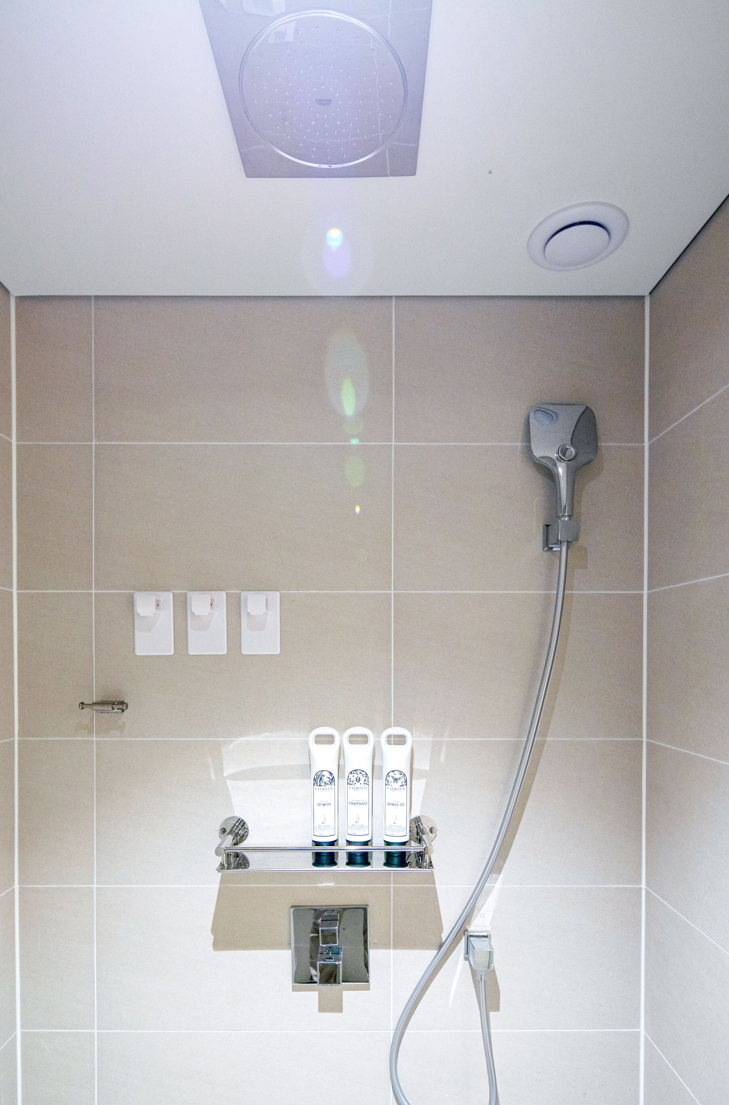 A shower area with a handheld showerhead, a wall-mounted control panel, and a shelf with toiletries.