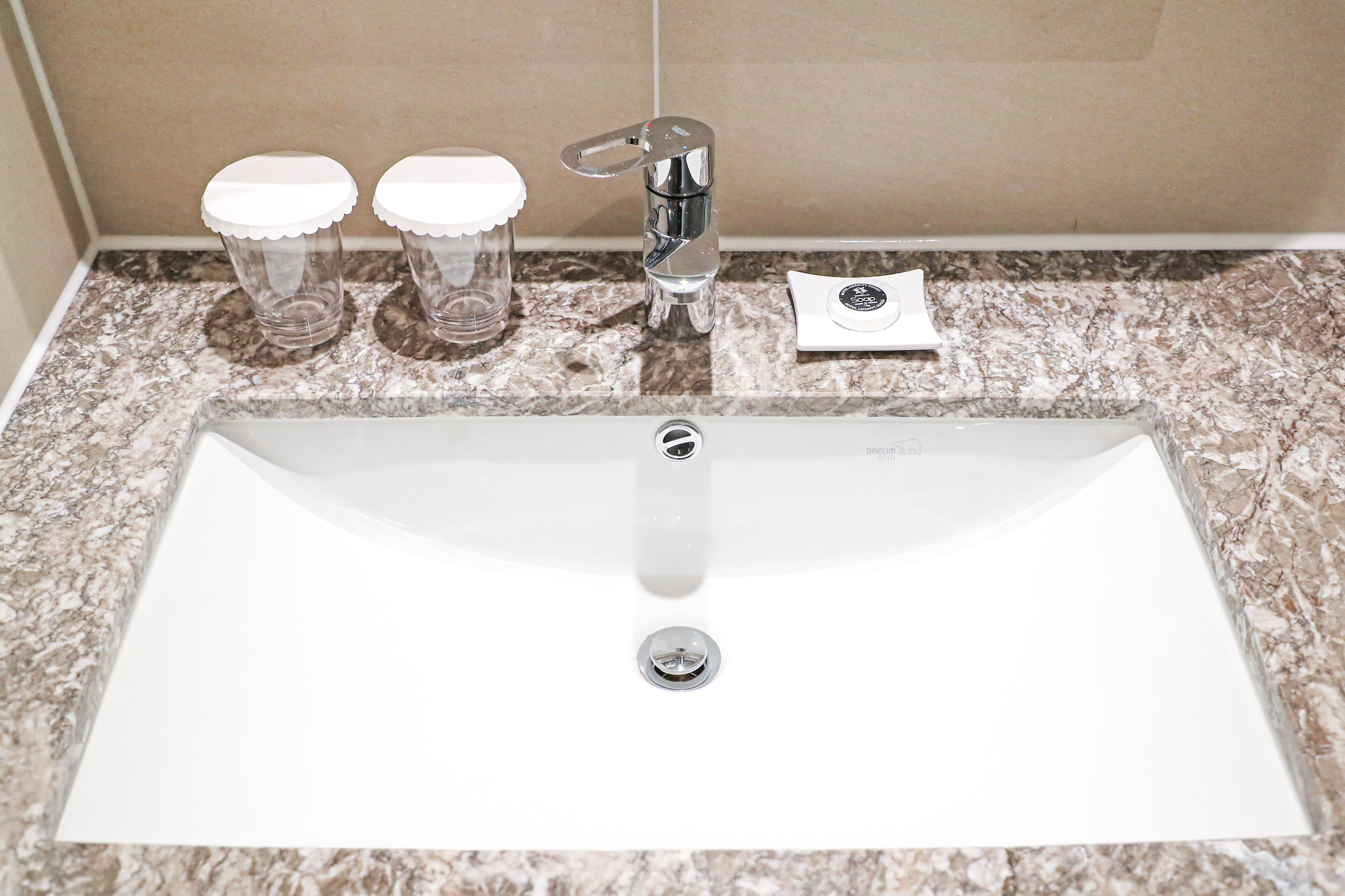 A bathroom sink with a chrome faucet, two clear glass containers with white lids, and a white towel on the countertop.