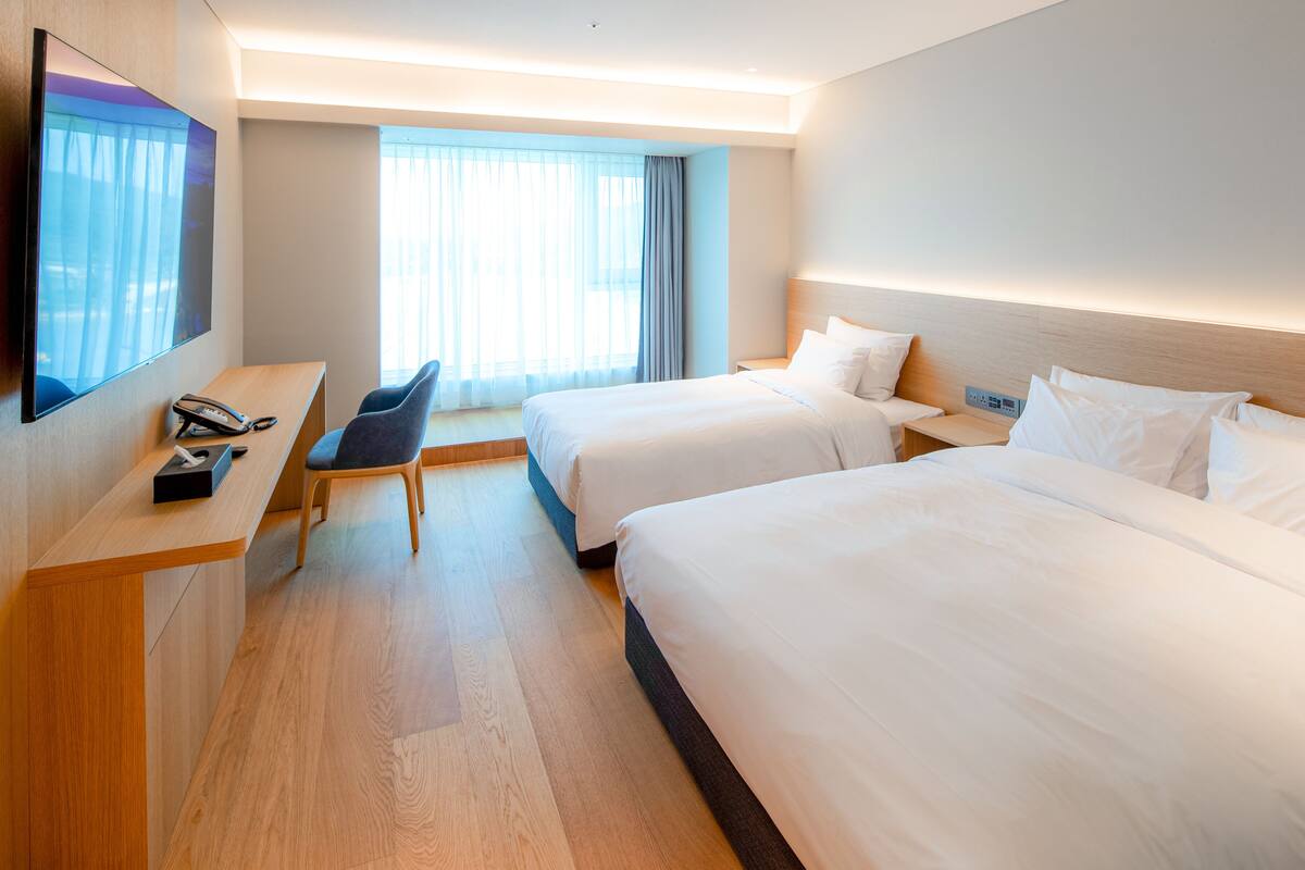Ein Hotelzimmer mit zwei Betten, einem Schreibtisch mit Telefon, einem Sessel und einem an der Wand befestigten Fernseher.