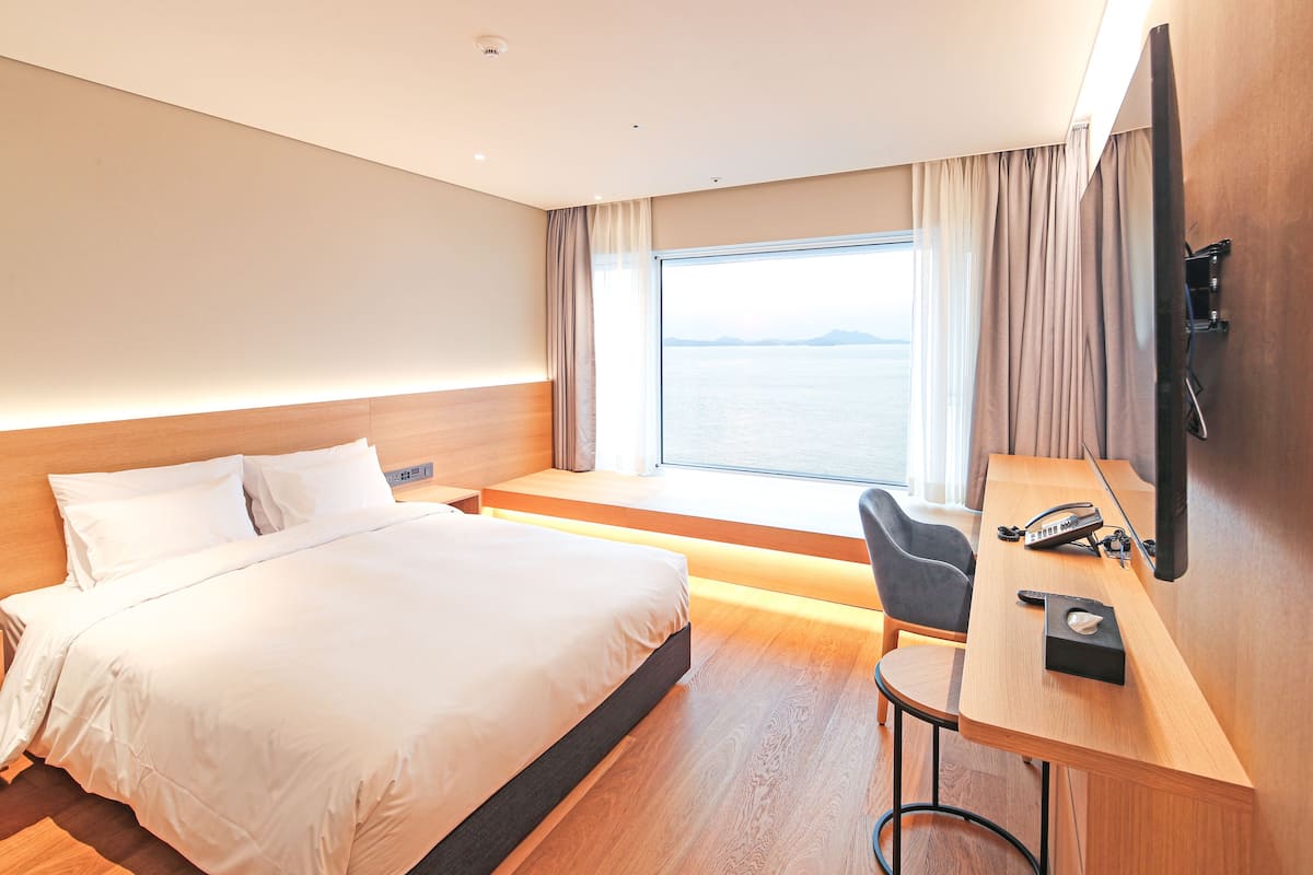 Ein modernes Hotelzimmer mit einem großen Bett, einem Schreibtisch mit Telefon und Meerblick.