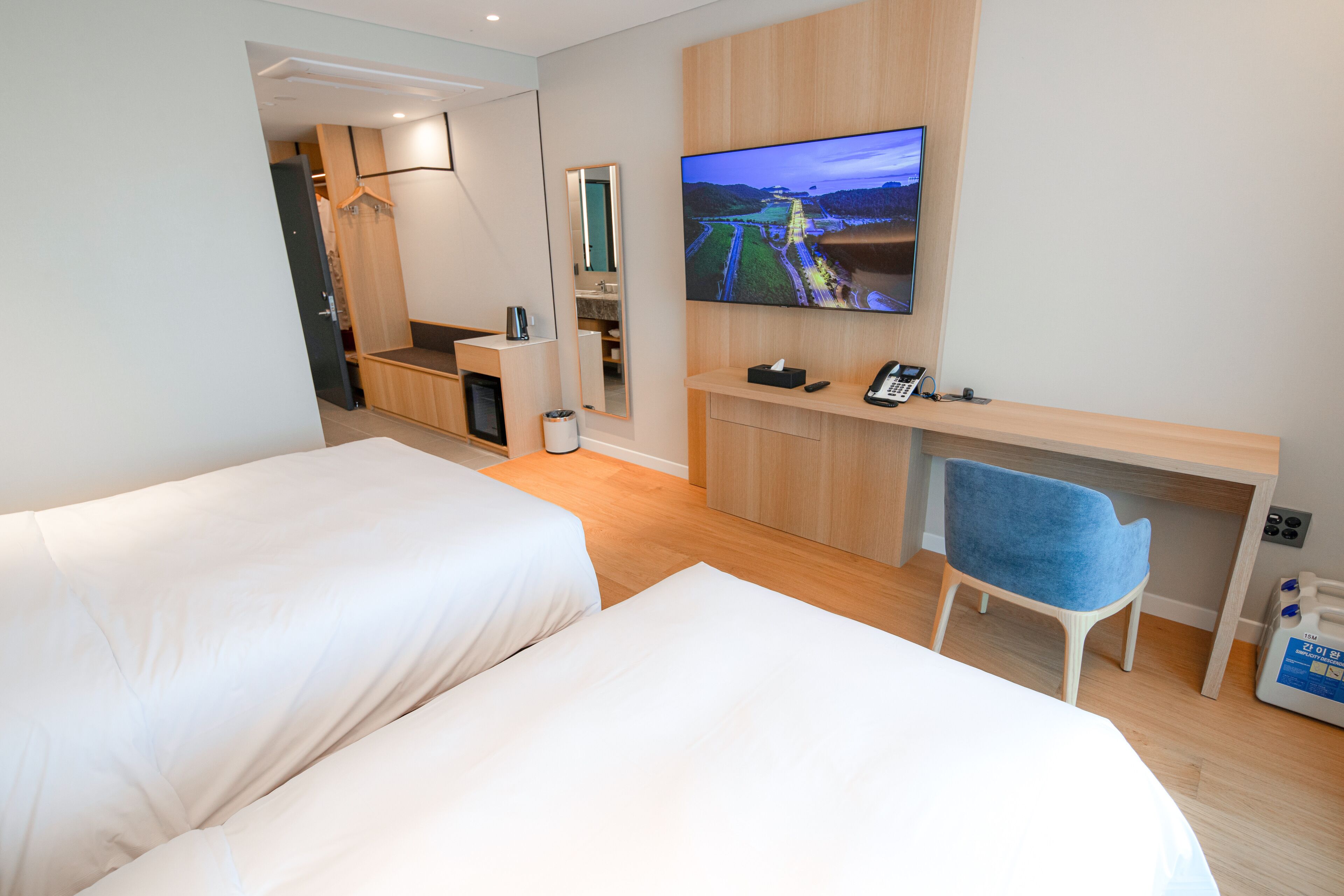 Een hotelkamer met twee bedden, een bureau met stoel, een televisie en een spiegel.