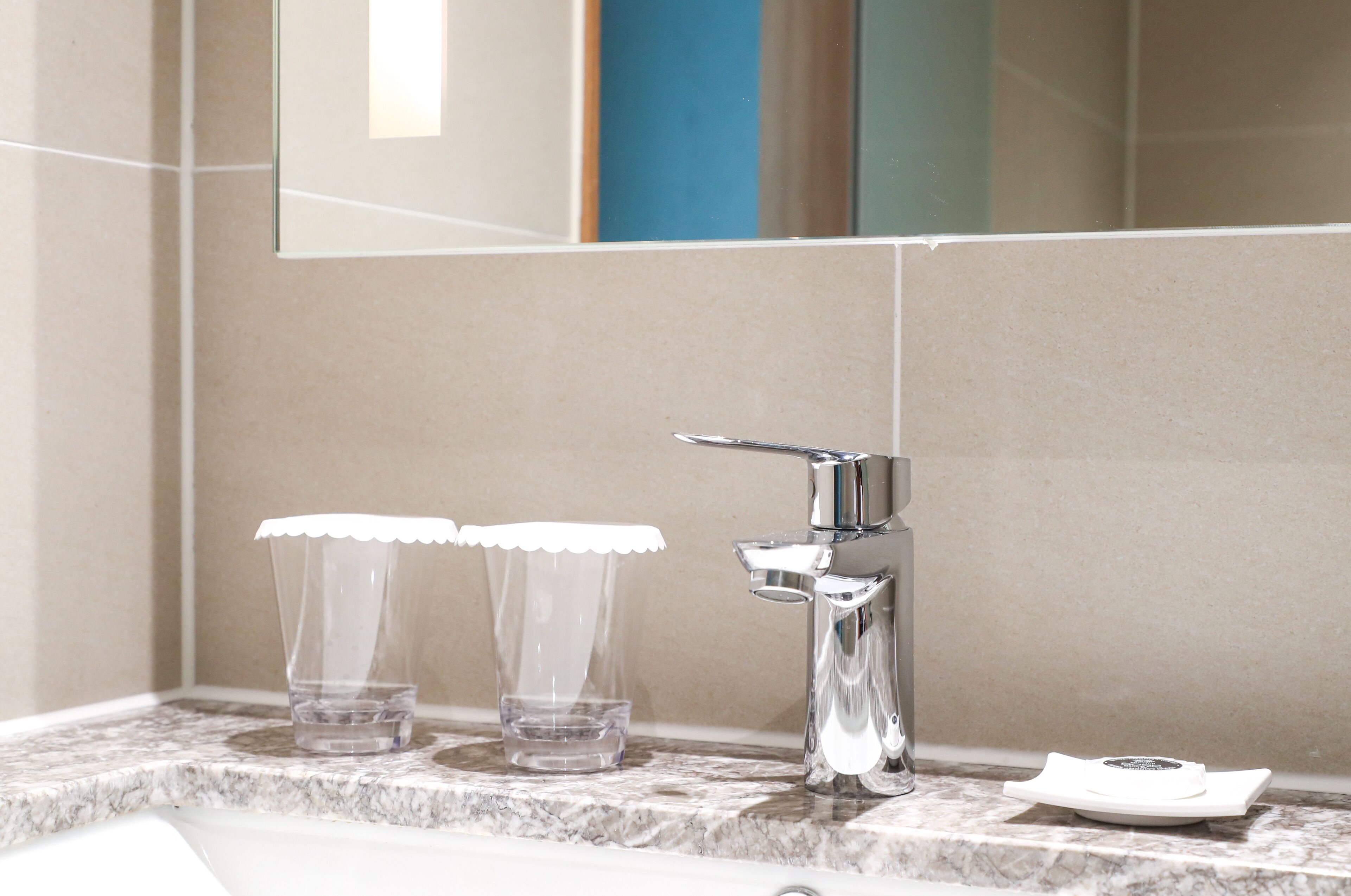 A bathroom with a marble countertop, a chrome faucet, and two clear glasses with lids.