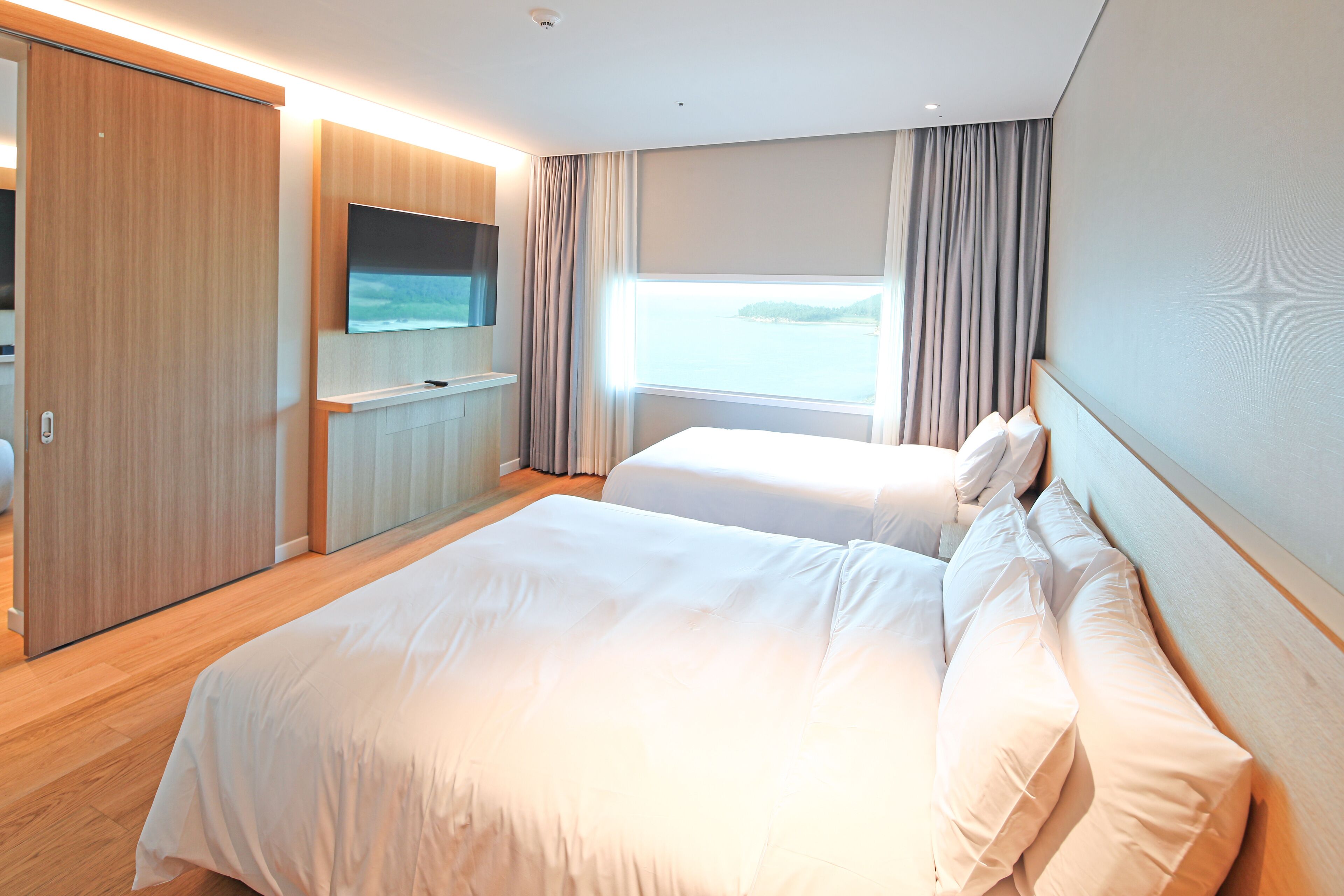 Een hotelkamer met een groot bed, een aan de muur bevestigde televisie en uitzicht op zee door het raam.