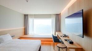 A hotel room with a bed, a desk with a chair, a telephone, and a large window with curtains. - HAENAM 126 HOTEL (Haenam)