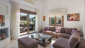 A spacious living room with a glass coffee table, two sofas, and a fireplace. - Villa Katerina (Chania)
