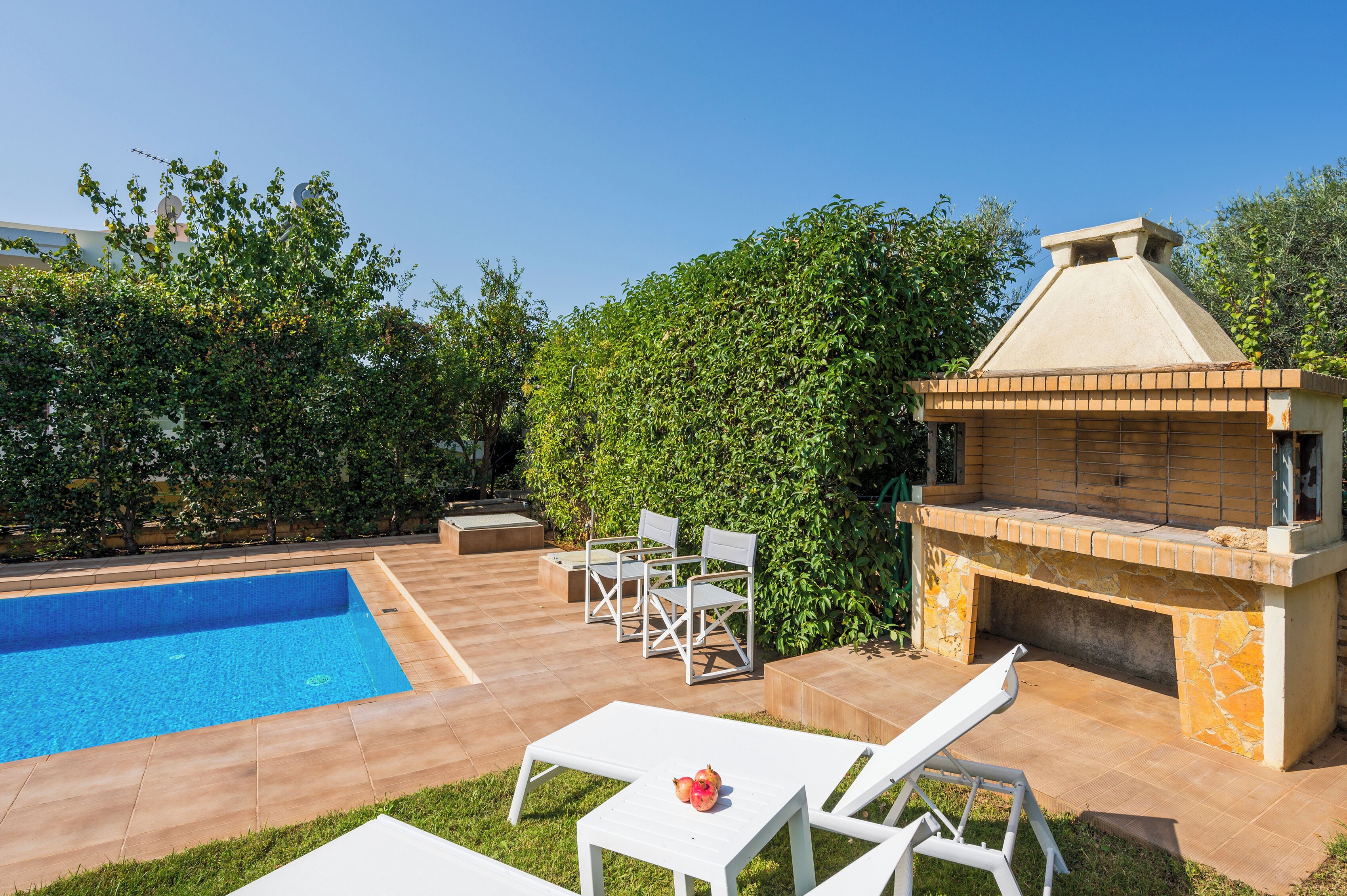 A swimming pool with a tiled deck, a barbecue area, and outdoor seating.