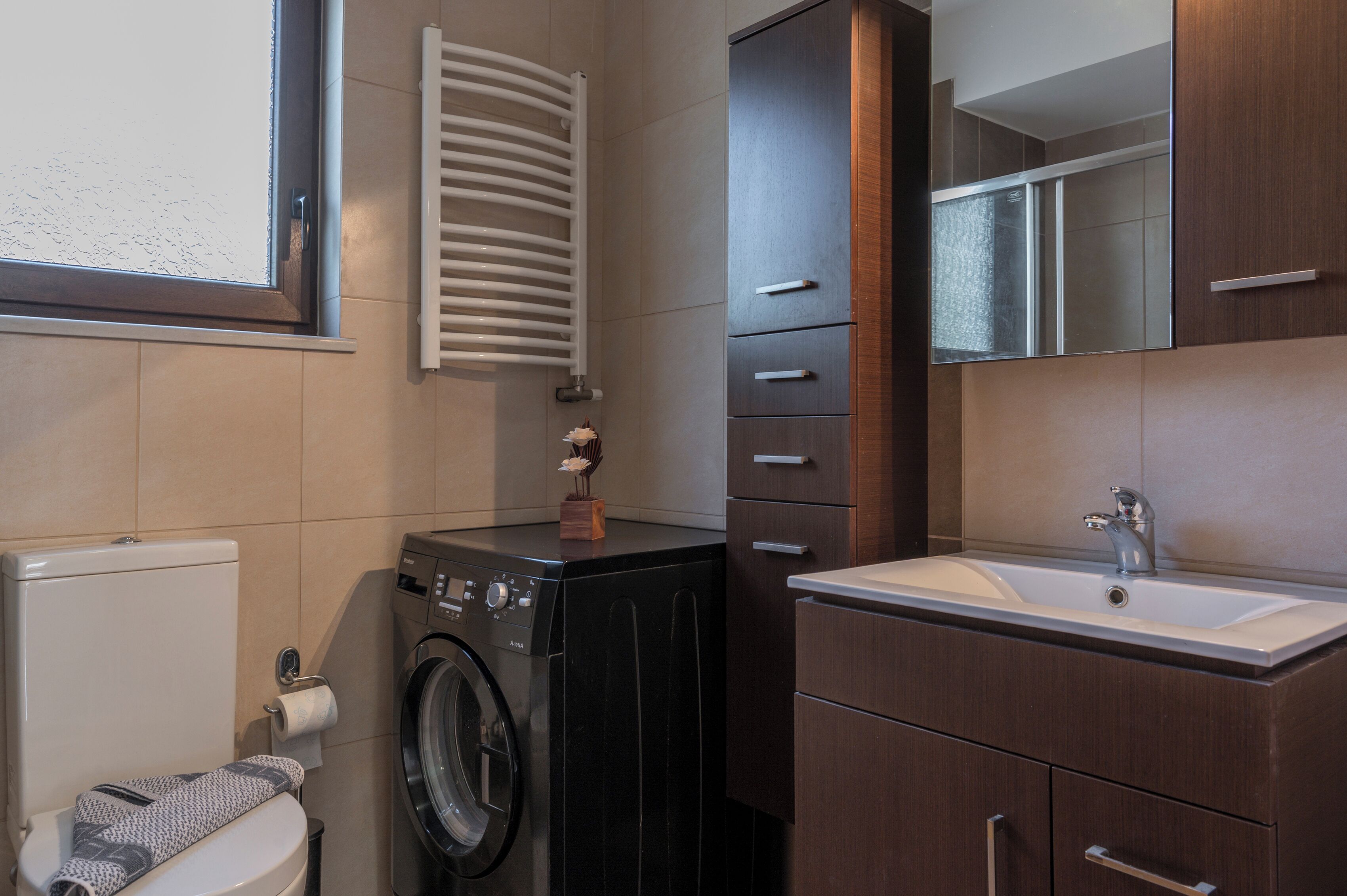 A compact bathroom with a washing machine, a toilet, a sink, and a mirror.