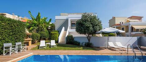 A swimming pool with lounge chairs, a small garden, and a modern building with a flat roof.