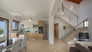 A modern kitchen with a dining area, a staircase, and a living room with a sofa. - Villa Katerina (Chania)