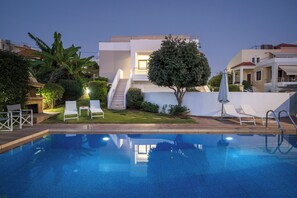 A modern pool area with a clear view of the pool, white lounge chairs, a staircase leading to a building, and surrounding greenery. - Villa Katerina (Chania)
