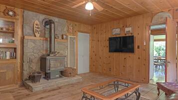 A cozy cabin interior with a stone fireplace, wooden walls, a ceiling fan, and a television mounted on the wall.