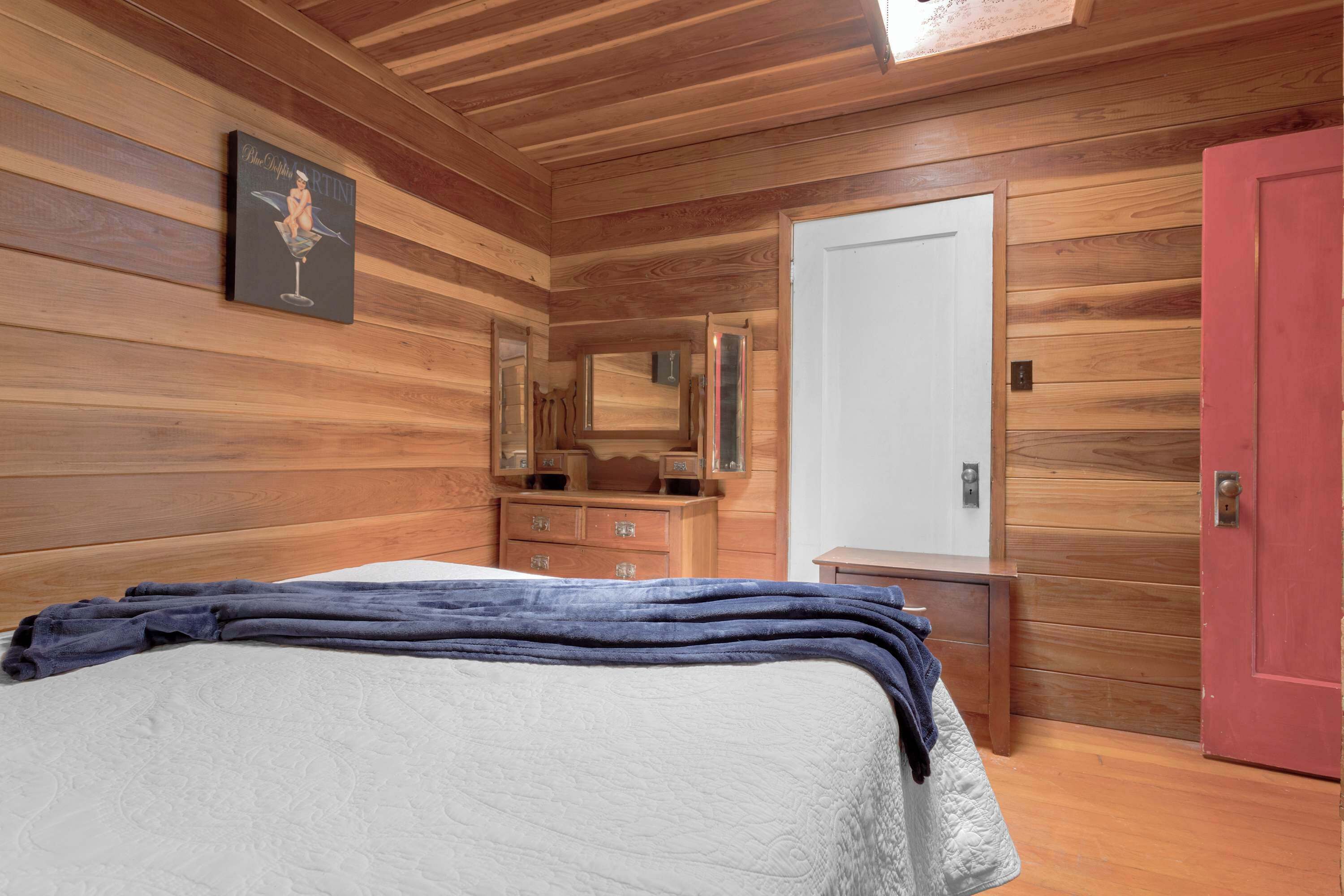 Een slaapkamer met houten lambrisering, een bed, een kaptafel en een rode deur.
