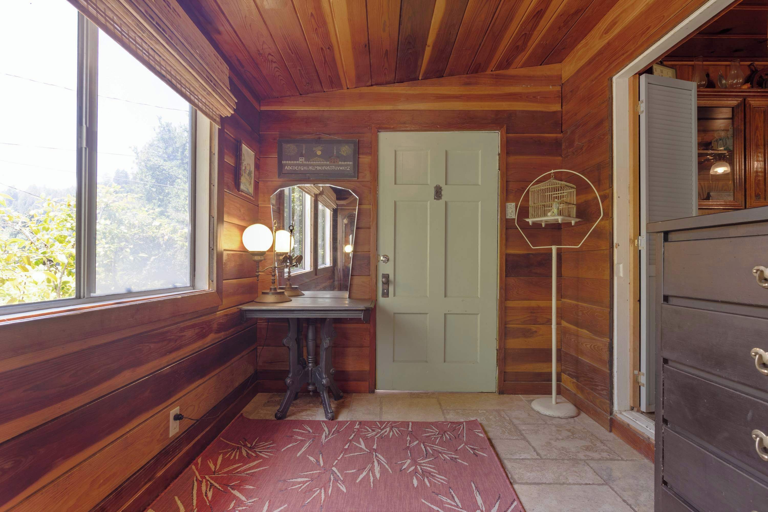 Un intérieur en bois avec une porte en bois, un miroir, une commode et une fenêtre.