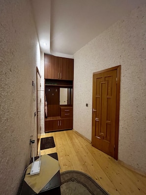 A narrow hallway with wooden flooring, a door on the right, and a small table with a device on it.