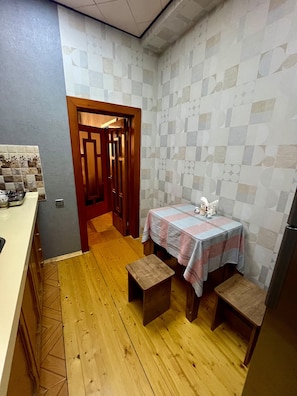 A compact kitchen with a wooden floor, a small table with a checkered tablecloth, and a door leading to another room.