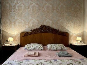 A neatly made bed with floral bedding, two nightstands with lamps, and a patterned wallpaper.