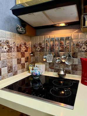 A kitchen with a black stovetop, a white countertop, and a backsplash with floral tiles.