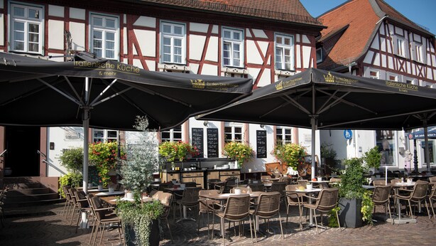 An outdoor café with tables and chairs, umbrellas, and potted plants. - Zu den drei Kronen (Seligenstadt)