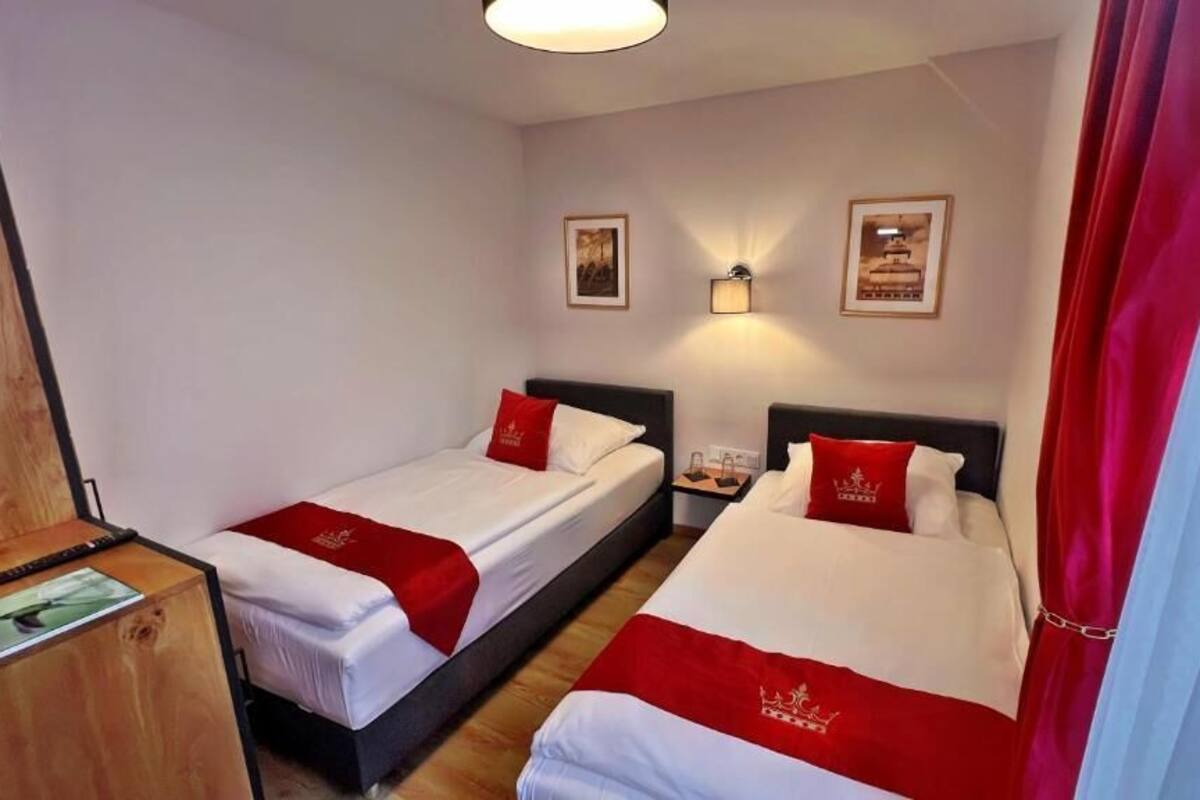 Habitación de hotel con dos camas, cada una con ropa de cama roja y blanca, un escritorio de madera y luces fijadas a la pared.